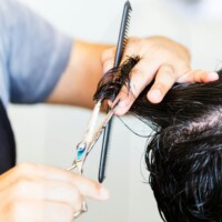 Strona główna Close-up of hairstylist cutting hair with scissors and comb, showcasing precise technique.