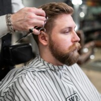 Strona główna A barber trims a bearded man's hair in a classic barbershop setting.